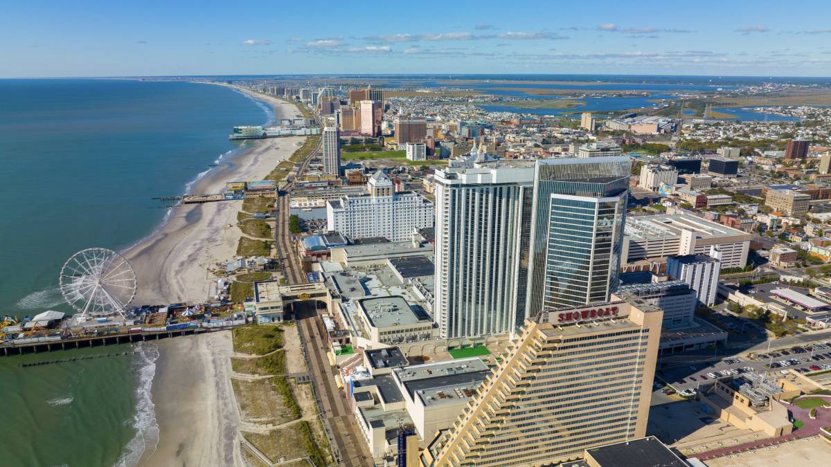 An aerial view in New Jersey map highlights the renewed political tension over proposed casino expansions beyond Atlantic City. Strong opposition arises from South Jersey leaders, who are mobilizing against plans to establish casinos in the northern or central state regions, such as the Meadowlands Sports Complex and Monmouth Park Racetrack. The background contrasts the traditional skyline of Atlantic City with potential new casino locations, emphasizing the regional divide. Speech bubbles from South Jersey leaders convey their concerns about economic impact and preservation of their local market.