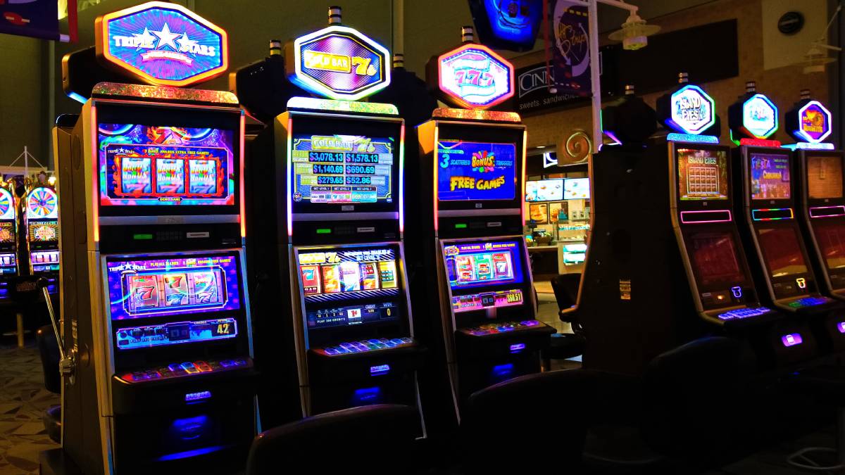A row of slot machines lined up inside a casino with bright digital displays and colorful lights. a new jersey woman may be forced to forfeit a jackpot she won at hollywood casino at penn national race course because she was on the state's self-exclusion list.