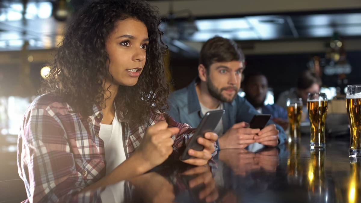 Friends using phones and computers to follow sports betting apps and live game odds.
