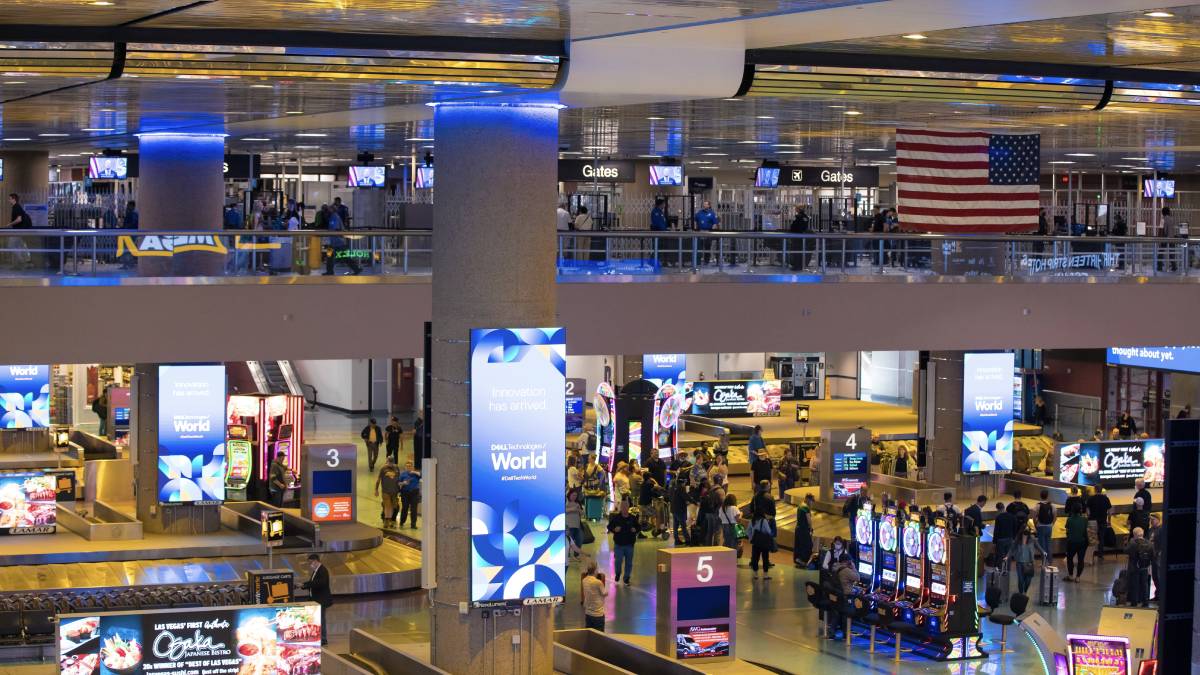 Passengers collecting luggage from a curved baggage carousel in the Las Vegas airport baggage claim area with the ticketing area above.